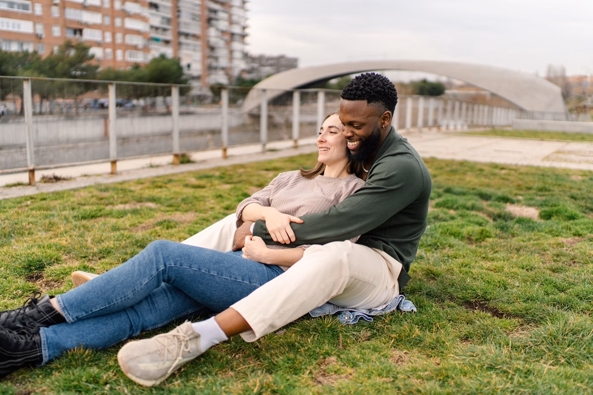 Jovem casal sorrindo deitado em grama ao ar livre - Metrópoles