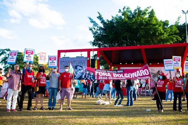Pessoas em frente a palco vermelho com faixas em gramado