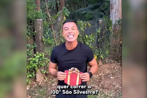 imagem colorida mostra homem segurando papel com desenho de presente e texto "quer correr a 100ª são silvestre?"