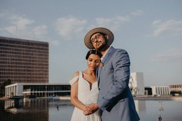 Foto de uma mulher vestida de branco e de um homem de chapéu abraçados