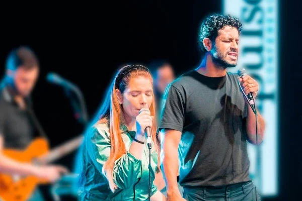 Na imagem colorida, cantora Camila Campos canta em microfone ao lado do marido, Léo Zagueiro - Metrópoles
