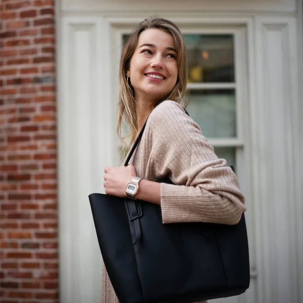 Foto de mulher branca e jovem, de cabelo liso loiro, posa para foto. Ela usa um casaco bege, uma bolsa de couro preta e um relógio dourado da marca Casio - Metrópoles