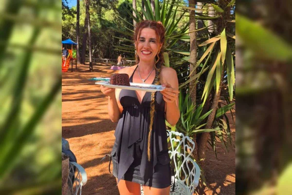 Mulher ruiva, de vestido preto, sorri segurando bolo de chocolate - Metrópoles