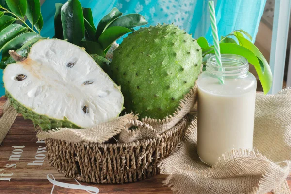 Imagem mostra uma graviola aberta e um copo de suco branco com canudo - Metrópoles