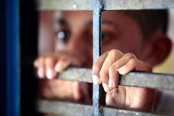 Menor infrator. Na imagem, um adolescente negro está segurando uma grade, em unidade socioeducativa - Metrópoles