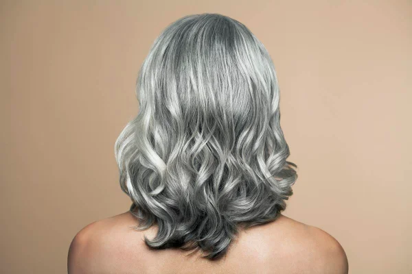 Foto colorida de uma mulher branca de cabelo grisalho de costas em um fundo bege - Metrópoles