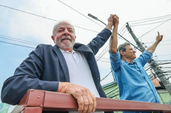 O candidato à presidência Lula e o candidato ao governo de São Paulo Haddad, ambos do PT, sorriem e erguem as mãos de cima de carreata em rua do estado - Metrópoles