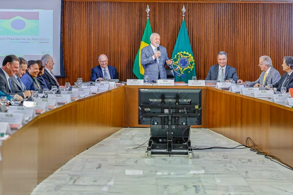 Imagem colorida do presidente Lula de pé com microfone. Ministros estão sentados na mesa ao redor - Metrópoles