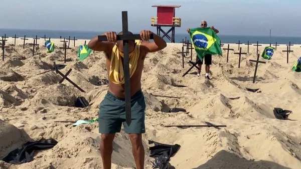 foto colorida de homem fincando cruz de madeira preta na areia da praia de Copacabana