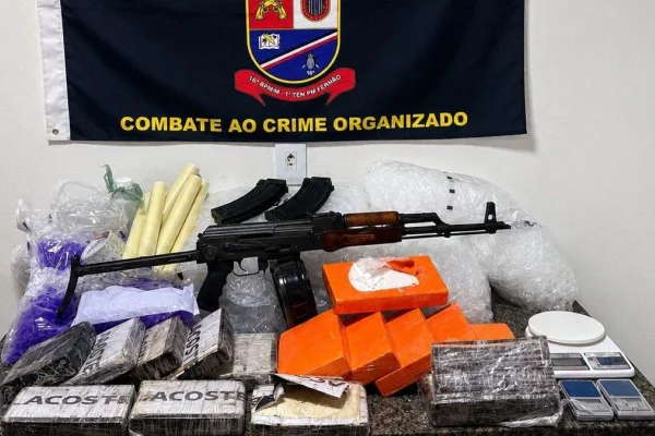 Imagens coloridas mostram fuzil e pacotes de drgas, dispostos em uma mesa preparada para entrevista à imprensa