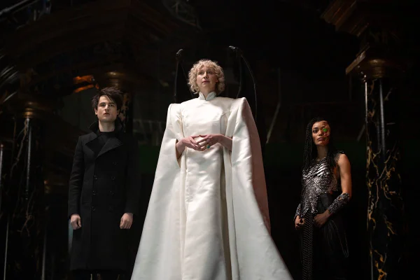 Série Sandman. Na imagem, mulher ao centro usa roupa branco com ombros marcados e caimento lateral, ao lado de homem com roupa preta e mulher com look prateado