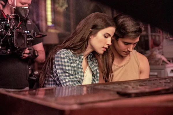 A atriz e cantora Giulia Be contracena com outro ator em cena de romance Depois do Universo, da Netflix. Atrás, um cinegrafista filma - Metrópoles