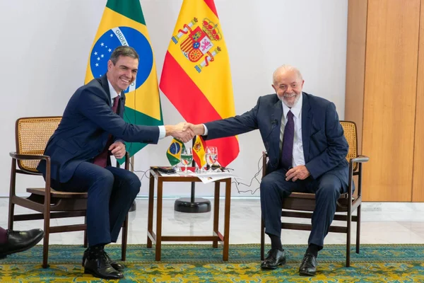 Imagem colorida do presidente Lula cumprimentando o presidente da Espanha com as bandeiras dos dois países atrás - Metrópoles