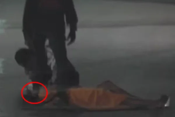 Imagem colorida de um homem com o pé em cima do pescoço de uma mulher deitada na rua - Metrópoles