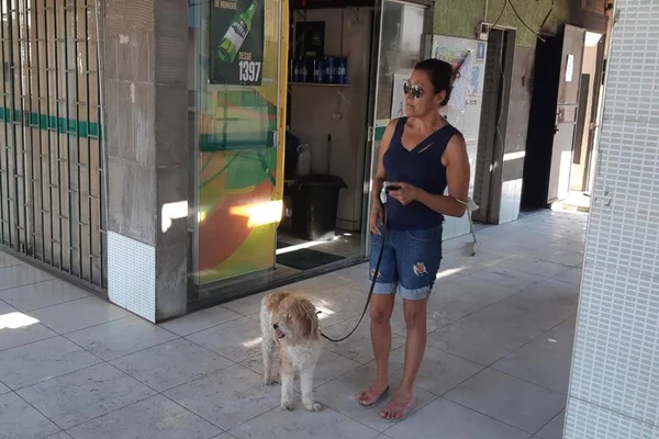 solange queiroz, mulher de bermuda jeans, blusa preta, acompanhada de cachorro branco e marro, preso por coleira