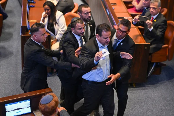 Imagem colorida de um membro do Knesset sendo retirado da Câmara após segurar uma placa em protesto durante um discurso do presidente dos EUA, Donald Trump, no Knesset, o parlamento israelense, em 13 de outubro de 2025, em Jerusalém.