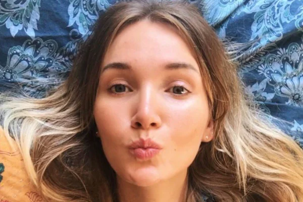 Mulher jovem,loira, deitada em superficie azul, fazendo pose para foto.