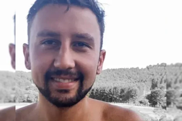 Homem branco de cabelos negros e barba sorri para foto
