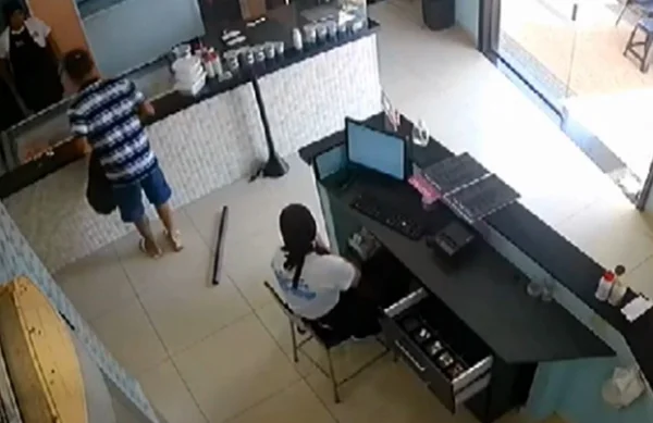 Imagem colorida mostra homem escolhendo sabor de sorvete enquanto assaltava sorveteria em Sertãozinho. O bandido veste camiseta com listras horizontais em azul e branco e bermuda azul, olhando para duas funcionárias que vestem roupa branca. Ele foi preso pela polícia - Metrópoles