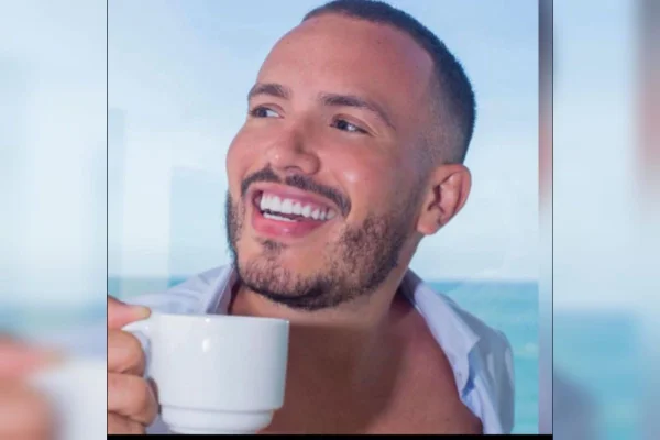 Homem branco com cabelo curto e barba sorri com xícara branca na mão direita - Metrópoles