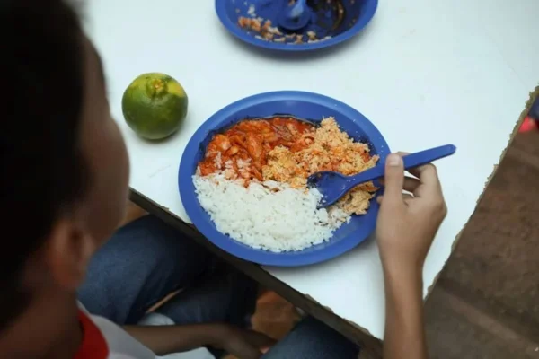 Imagem colorida mostra criança comendo merenda escolar - Metrópoles
