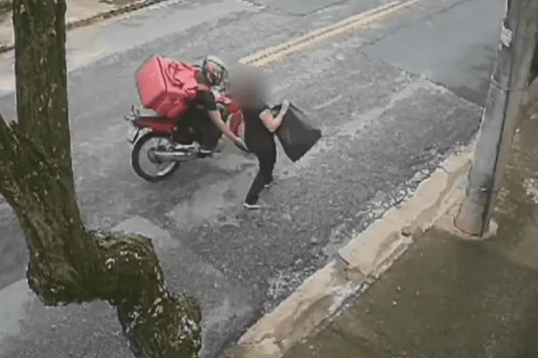 Imagem colorida de uma câmera de segurança, a qual mostra um motoboy se aproximando e apalpando a bunda de uma mulher no meio da rua - Metrópoles
