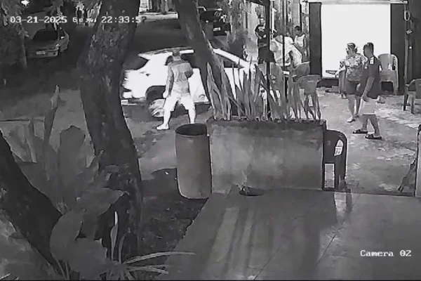 Captura de tela, em preto de branco, de câmera de segurança que mostra motorista de aplicativo, em um carro branco, jogando o veículo contra grupo de pessoas em frente a bar no Rio de Janeiro. - Metrópoles