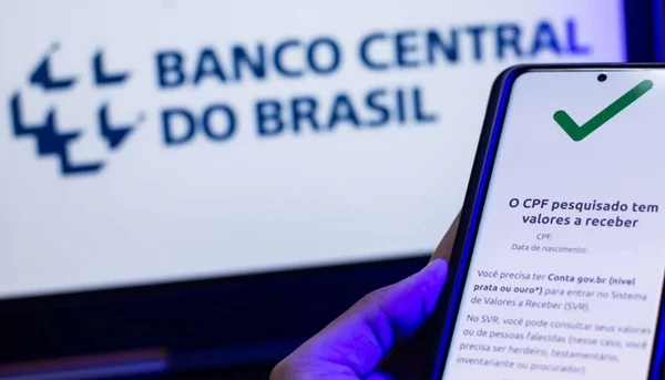 imagem colorida de uma mão segurando um celular para consultar dinheiro esquecido no Banco Central