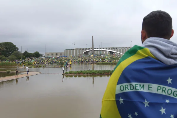 foto colorida. Homem com a bandeira do Brasil nas costas virado para o QG do Exercito