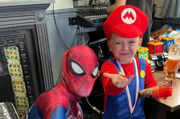Imagem mostra criança branca vestida de personagem do Mario Bros posando com o personagem homem-aranha - Metrópoles
