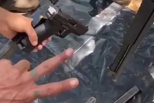Mão fazendo V de vitória ao lado de outra segurando pistola - Metrópoles