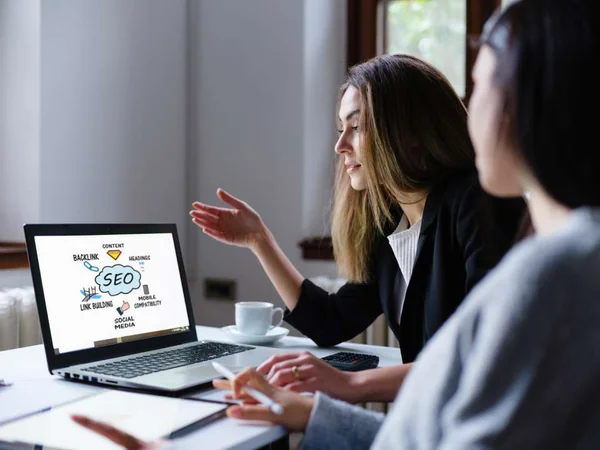 Na foto há duas mulheres olhando para o computador - Metrópoles