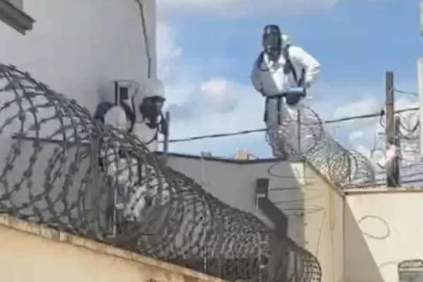 Imagem colorida de bombeiros com roupa especial em cima de telhado. Metrópoles