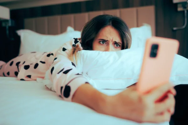 Mulher deitada na cama com o celular nas mãos