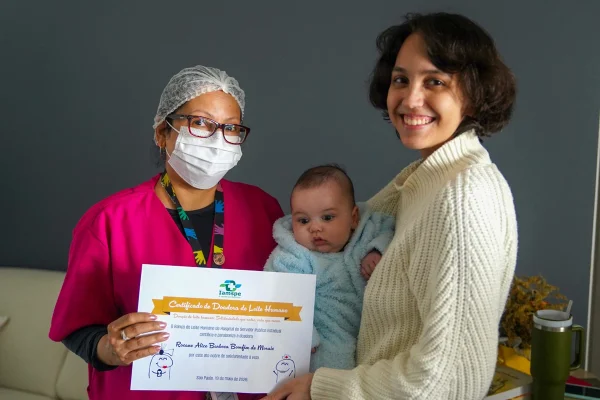 Foto colorida de duas mulheres e um bebê segurando um certificado - Metrópoles.