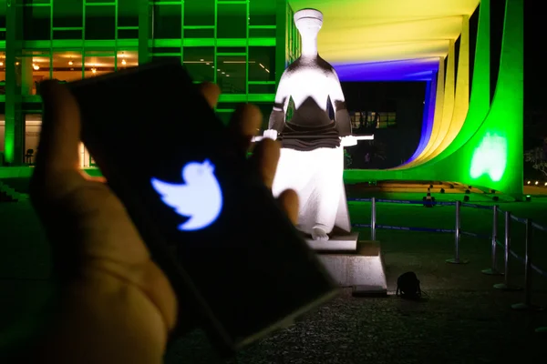 Celular com imagens do site e logo do Twitter em frente ao STF