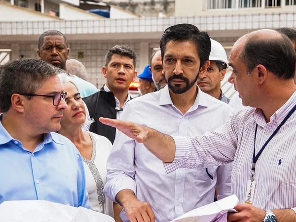 Imagem colorida mostra Ricardo Nunes, homem branco de cabelo e barba pretos, vestindo camisa branca, cercado de outros homens gesticulando com as mãos, em uma visita a obra pública - Metrópoles