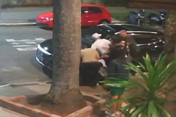 Imagem colorida de homem se aglomerando ao lado de carro preto, de noite, ao lado de restaurante - Metrópoles