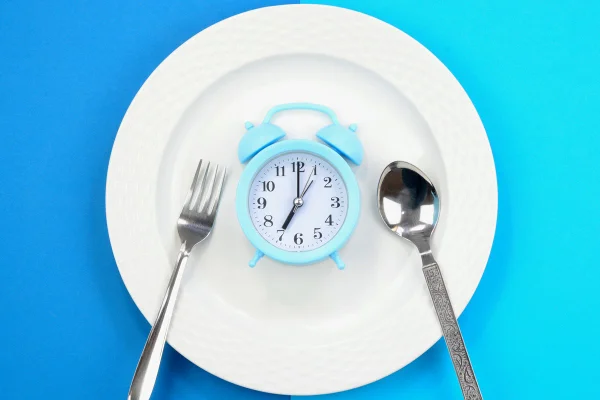 Conceito de dieta e perda de peso. Despertador em um prato branco. Jejum. Metrópoles