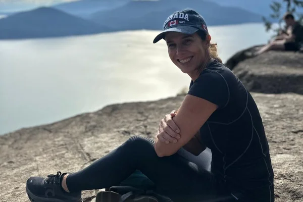 Foto colorida de mulher sentada em ambiente aberto, com fundo que mostra um lago/rio - Metrópoles.