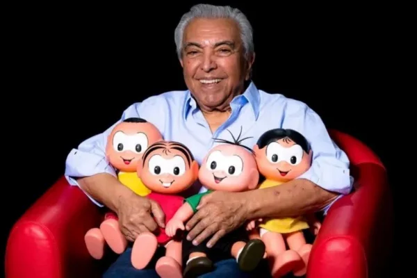 Mauricio de Souza, um homem com baleo grisalho e sobrancelhas pretas, usa camisa azul clara e segura quatro bonecos de personagens da Turma da Mônica no colo - Metrópoles