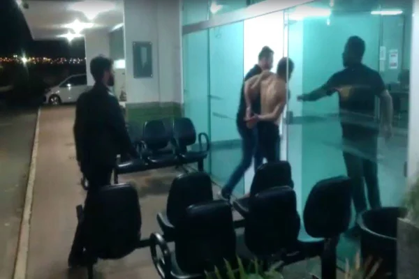 Policiais carregam suspeito sem camisa para delegacia