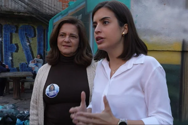 Imagem colorida mostra candidatas à prefeita e vice-prefeita, Tabata Amaral e Lúcia França, lado a lado em frente a muro de escola municipal de São Paulo. Tabata usa uma camisa branca, tem cabelo preto e pele branca. Lúcia veste uma blusa de frio escura, com um casaco de cor bege por cima. Lucia também é branca, tem cabelo castanho de tamanho médio e liso. metrópoles
