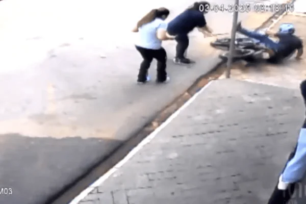 Imagem colorida de uma câmera de segurança mostra uma mulher de camiseta preta com um pedaço de ferro agredindo um assaltante, que cai de moto na calçada - Metrópoles