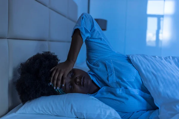 Imagem mostra mulher negra deitada de pijama na cama com a mão na cabeça - Metrópoles - dormir