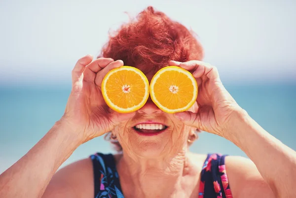 Mulher idosa de cabelo ruivo segurando duas fatias de laranja cortadas nos olhos - Metrópoles - longevidade espermidina genética boa, longevidade