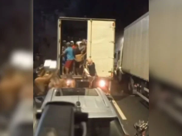 Imagem colorida mostra grupo de pessoas cercando um caminhão com a área de carga aberta sendo saqueado - Metrópoles