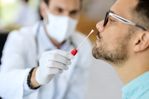 Imagem colorida mostra médico fazendo teste para detecção de covid em um homem que usa óculos - Metrópoles