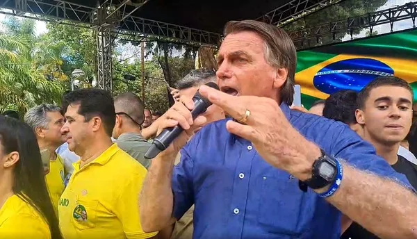 O presidente e candidato à reeleição Jair Bolsonaro discursa com microfone na mão em evento na cidade de Teófilo Otoni (MG). Várias pessoas o cercam e uma bandeira do Brasil aparece no telão atrás - Metrópoles