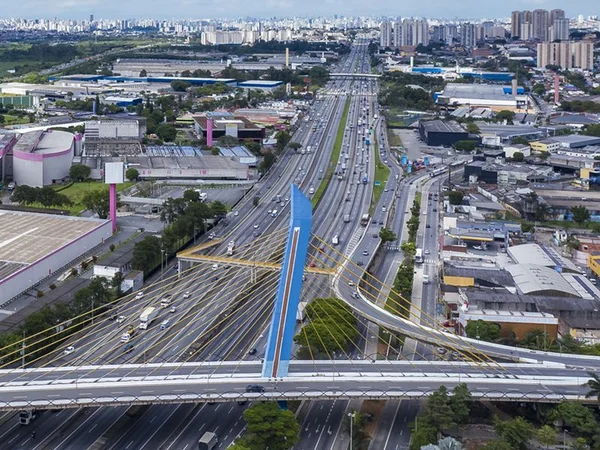 Imagem aérea colorida da Rodovia Presidente Dutra, na altura da cidade de Guarulhos, com a ponte de acesso à cidade, azul, em primeiro plano - Metrópoles